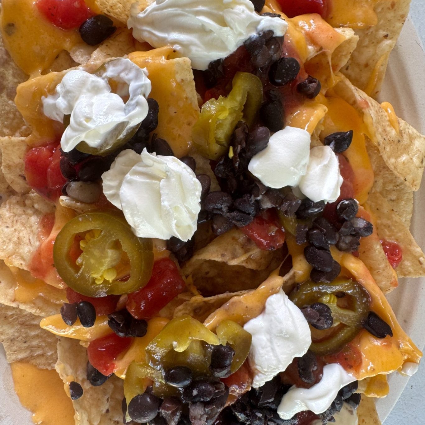 Plate of nachos topped with cheese, sour cream, black beans, jalapeños, and diced tomatoes.
